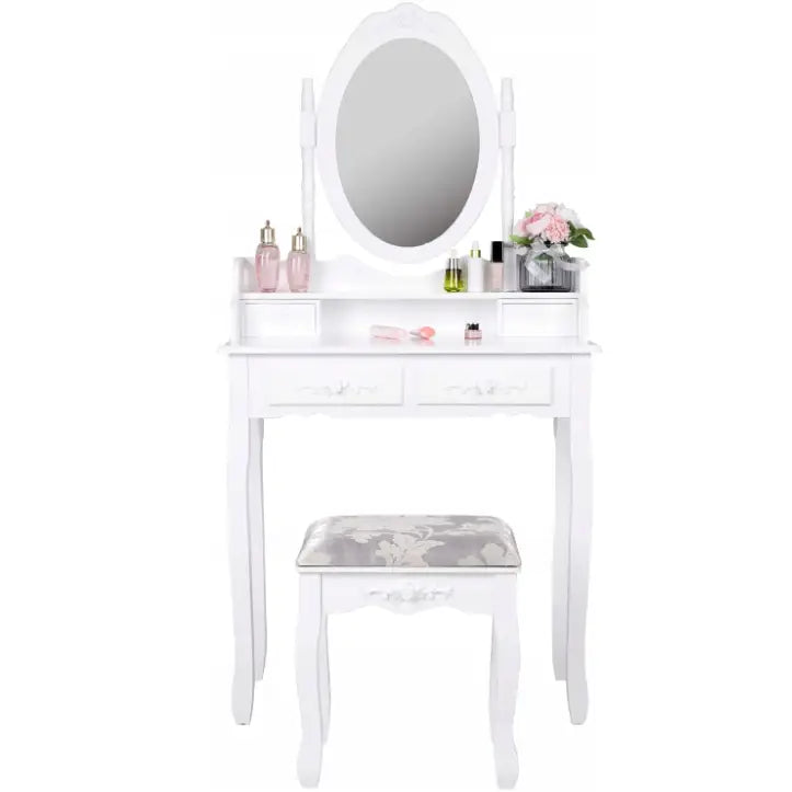 Sminkebord med ovalt speil og hvit krakk, sett forfra med sminke, flasker og blomster på bordplaten.