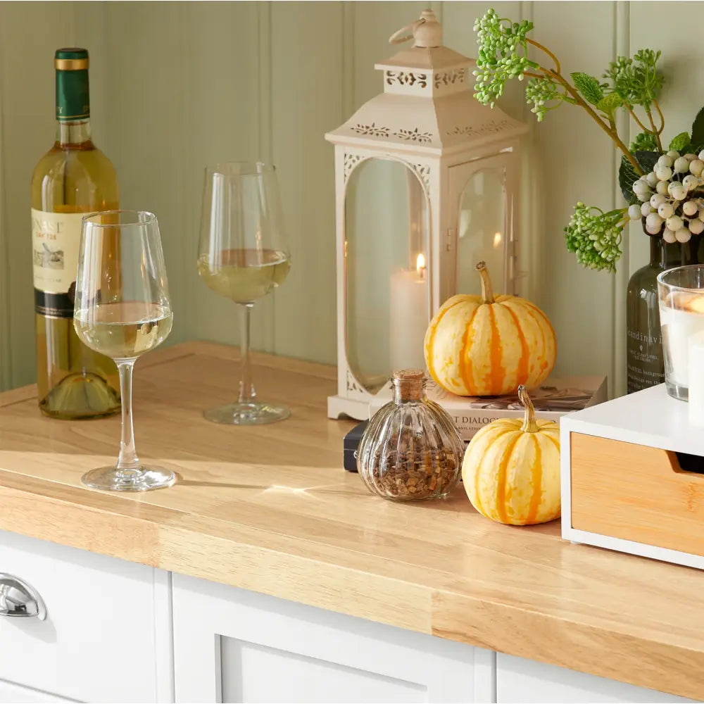 Sobuy kjøkkenøy i lyst tre, dekorert med vin, gresskar, tent lykt og grønne planter for lun atmosfære.