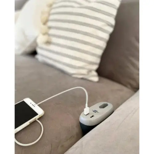 Sofa Lader USB estilo, hvit mobiltelefon lades med hvit kabel fra grå ladeenhet i grå sofakrok.
