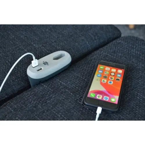 Sofa Lader USB, grå ladeenhet med USB-port koblet til svart sofa, sett skrått ovenfra med tilkoblet smarttelefon.