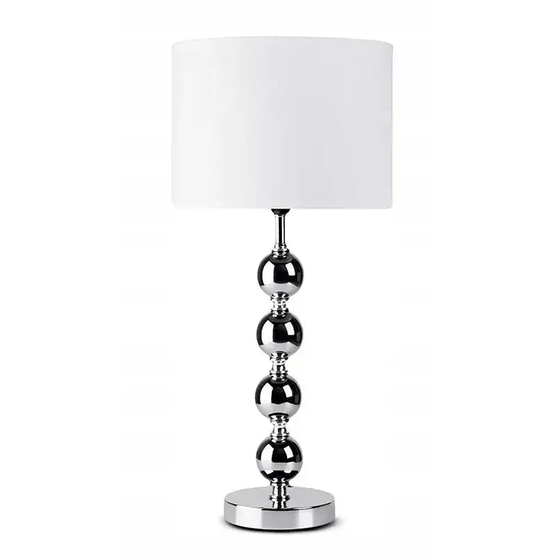 Sølvhvit bordlampe med sylinderformet skjerm og fot av fire blanke metallkuler, sett forfra.