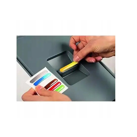 Søppelbøtte for sortering, toppvisning der en gul etikett settes på lokket, flere etiketter vises i hånden.