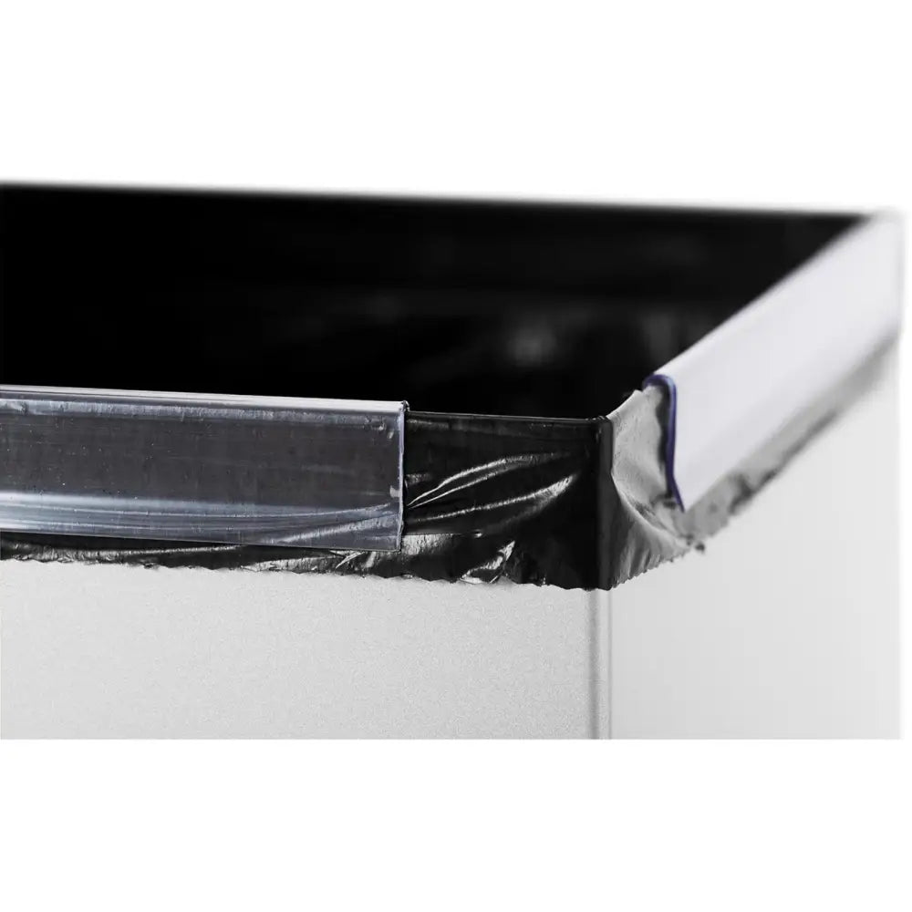 Søppelbøtte i stål, nærbilde av hjørne med sort pose under klar plastrimme mot sølvfarget overflate.