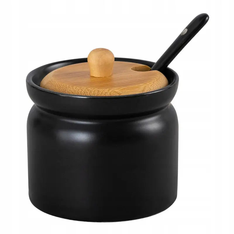 Sort sukkerboks i matt keramikk med bambuslokk og treskje med sort håndtak, sett fra skrå vinkel.