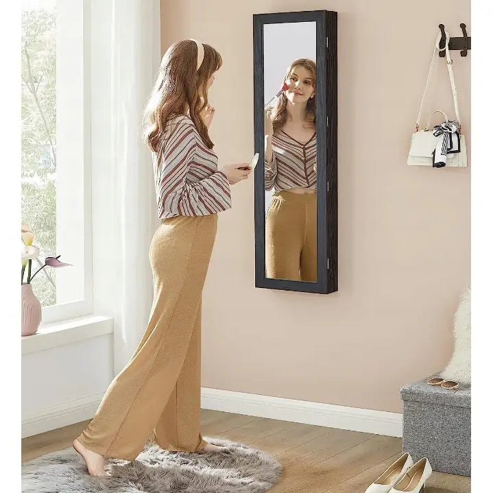 Speil smykkeskap veggmontert i sort, sidevisning med person som sminker seg i et lyst rom.