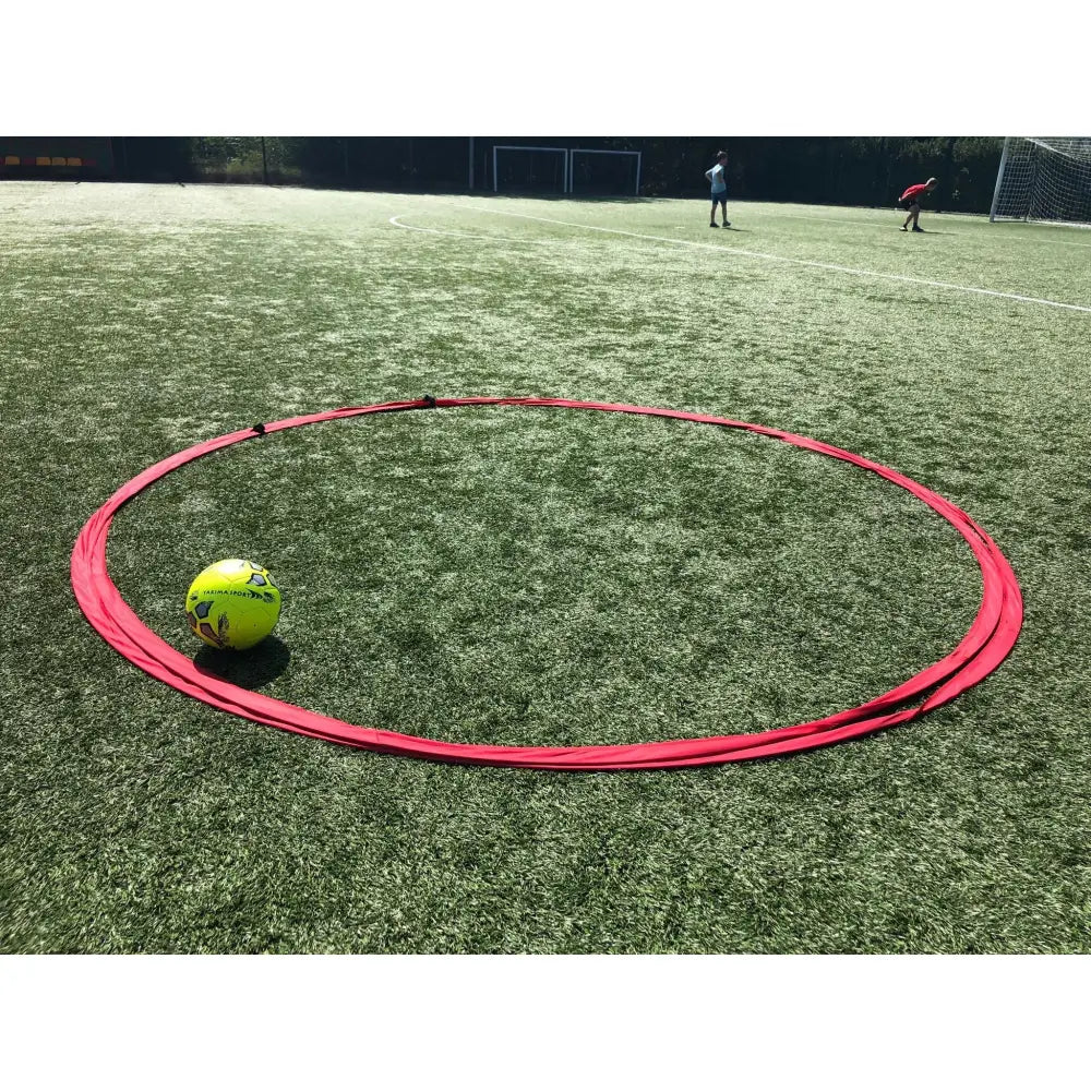 Spillet hjul Tiki Taka, rød ring på kunstgress med gul fotball innenfor og mål i bakgrunnen.