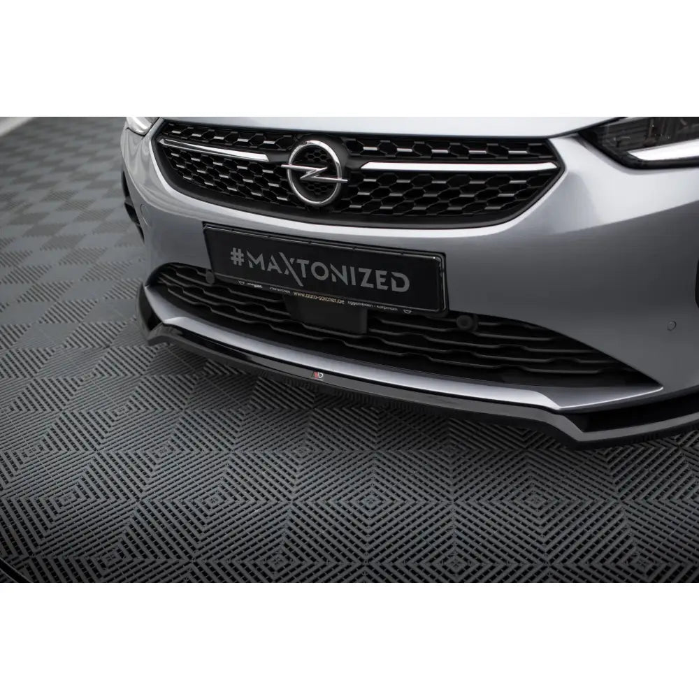 Spoiler på Opel Corsa F V2, sort frontsplitter montert på sølvfarget bil mot sportslig underlag.