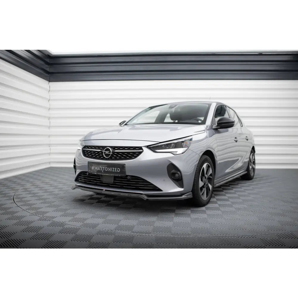 Front splitter montert på Opel Corsa F V2, sølvfarget bil med svarte felger, sett skrått forfra innendørs.