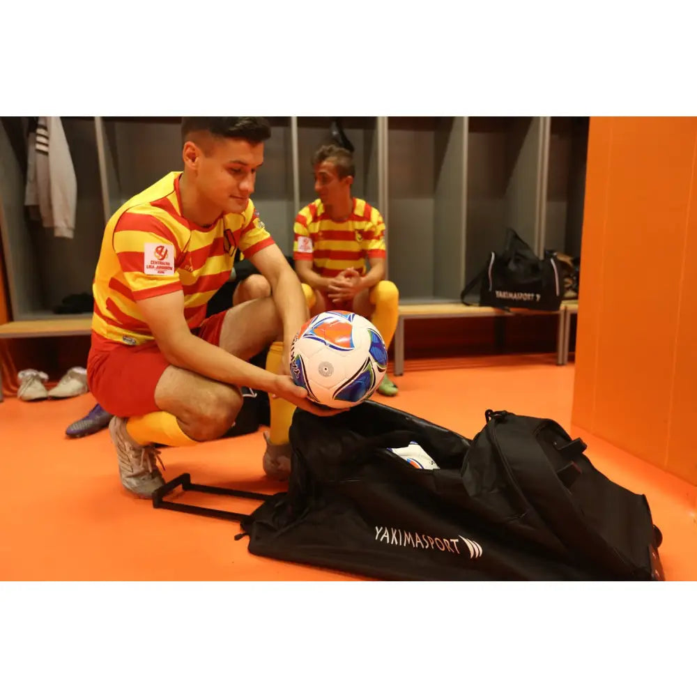 Sportbag på hjul fra YAKIMASPORT, åpen i garderobe, spiller legger fotball oppi bagen.