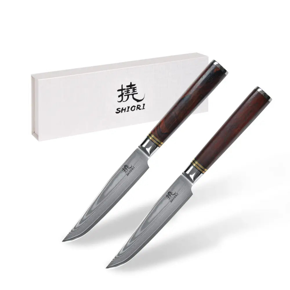 Steakkniver Shiori med damaskmønstret blad og mørkt trehåndtak foran gaveeske med logo.