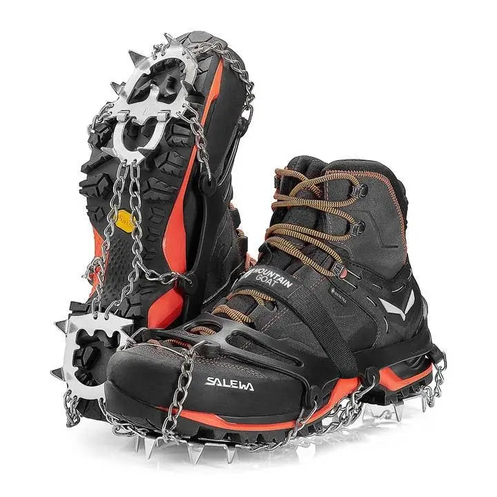 Stegjern med 13 tagger for fjellsko, viser stålpigger og kjetting under sorte støvler med oransje detaljer.