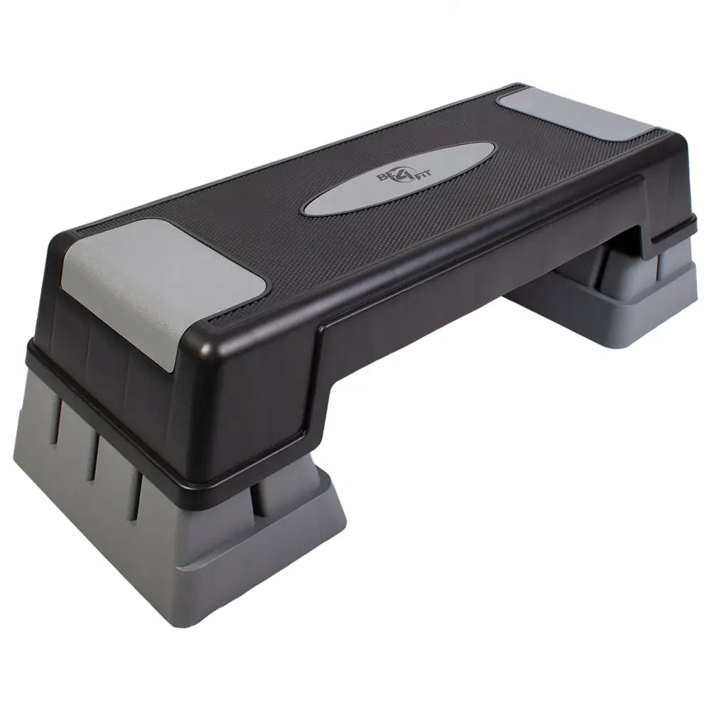 Stepbenk til aerobic, sort og grå med rillet overflate, sett fra siden med synlige justerbare høyder.