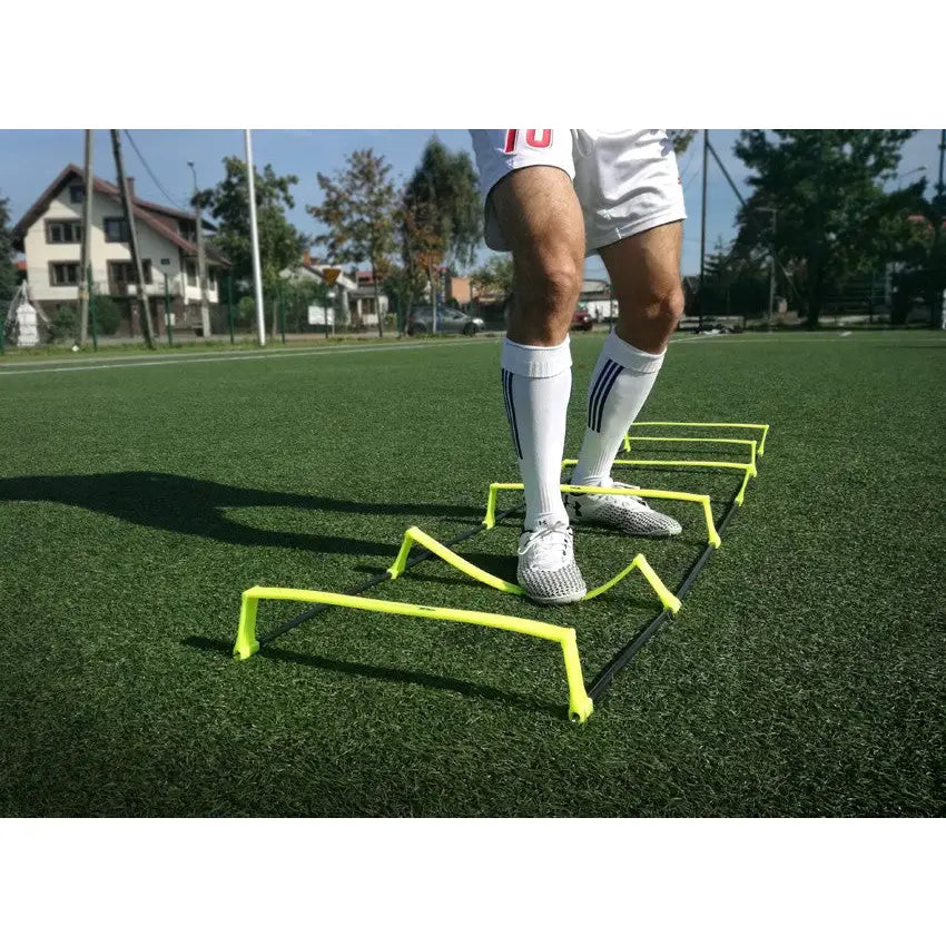 Stige med 10 trinn i neongult plast, brukt til fotballtrening på gress, sett fra lav vinkel nær bakken.