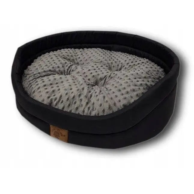 Stoff hundeseng størrelse L, rund med svart høy ramme, grå prikkete pute og brun etikett synlig foran.