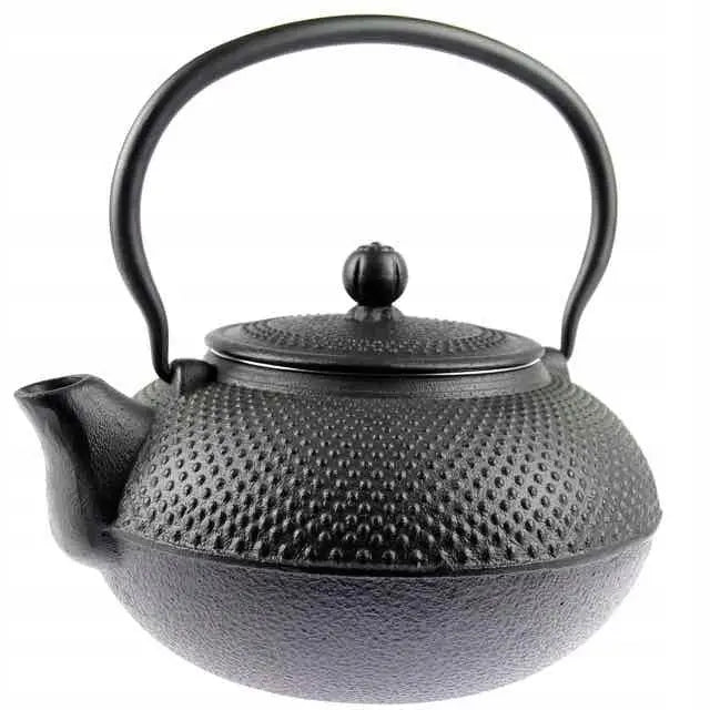 Støpejern tekanne med prikkete overflate, stor rund hank og dekorativ kule på lokket, skrå frontvisning.