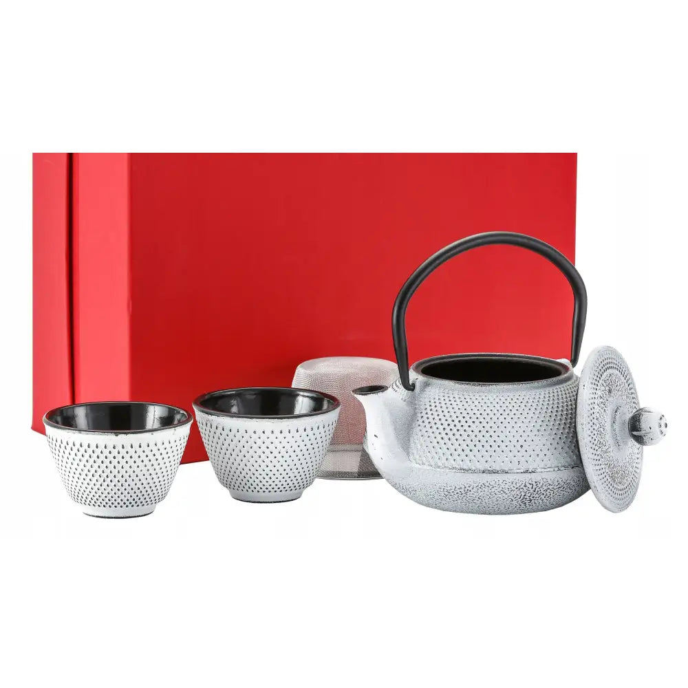 Støpejernskanne med to grå tekopper, sort hank og tefilter, plassert foran rød gaveeske.