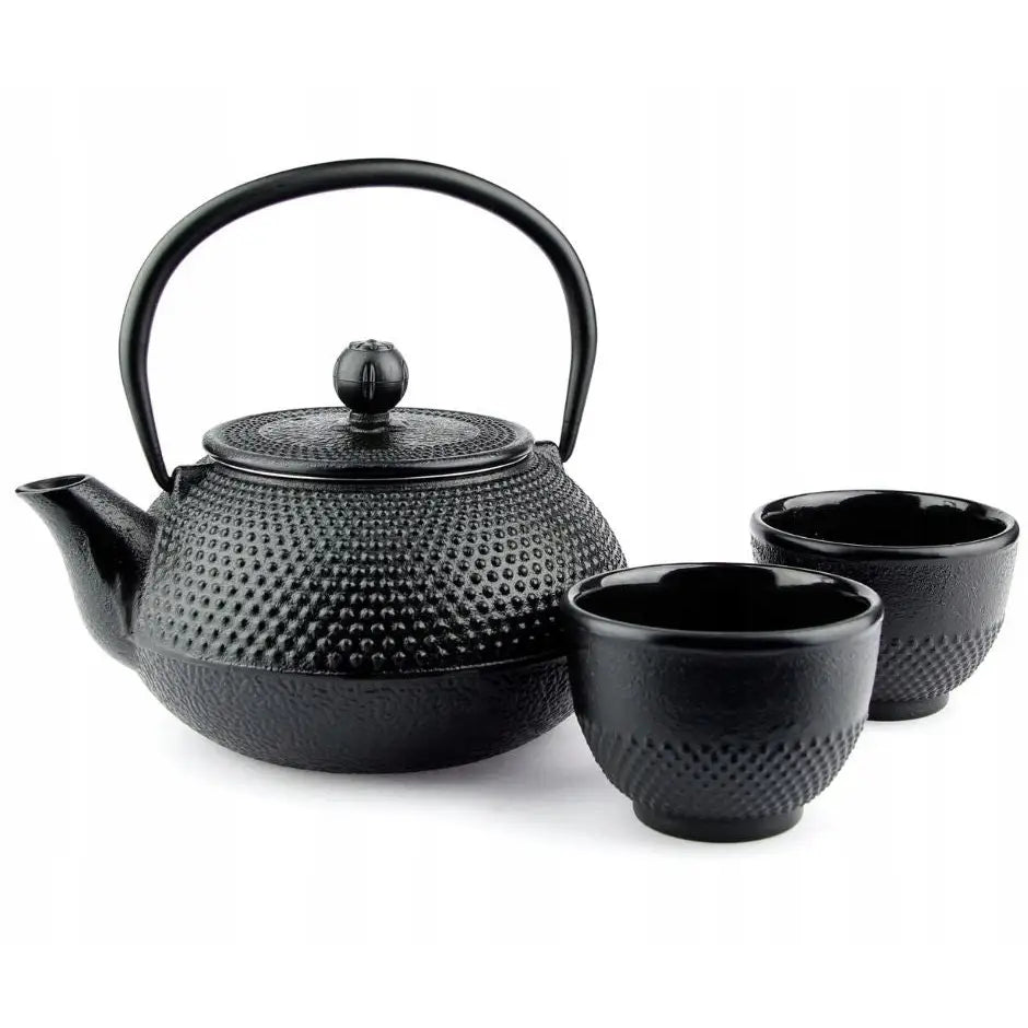 Støpejernste-sett med sort tekanne og to kopper, prikkete overflate, frontvisning mot hvit bakgrunn.