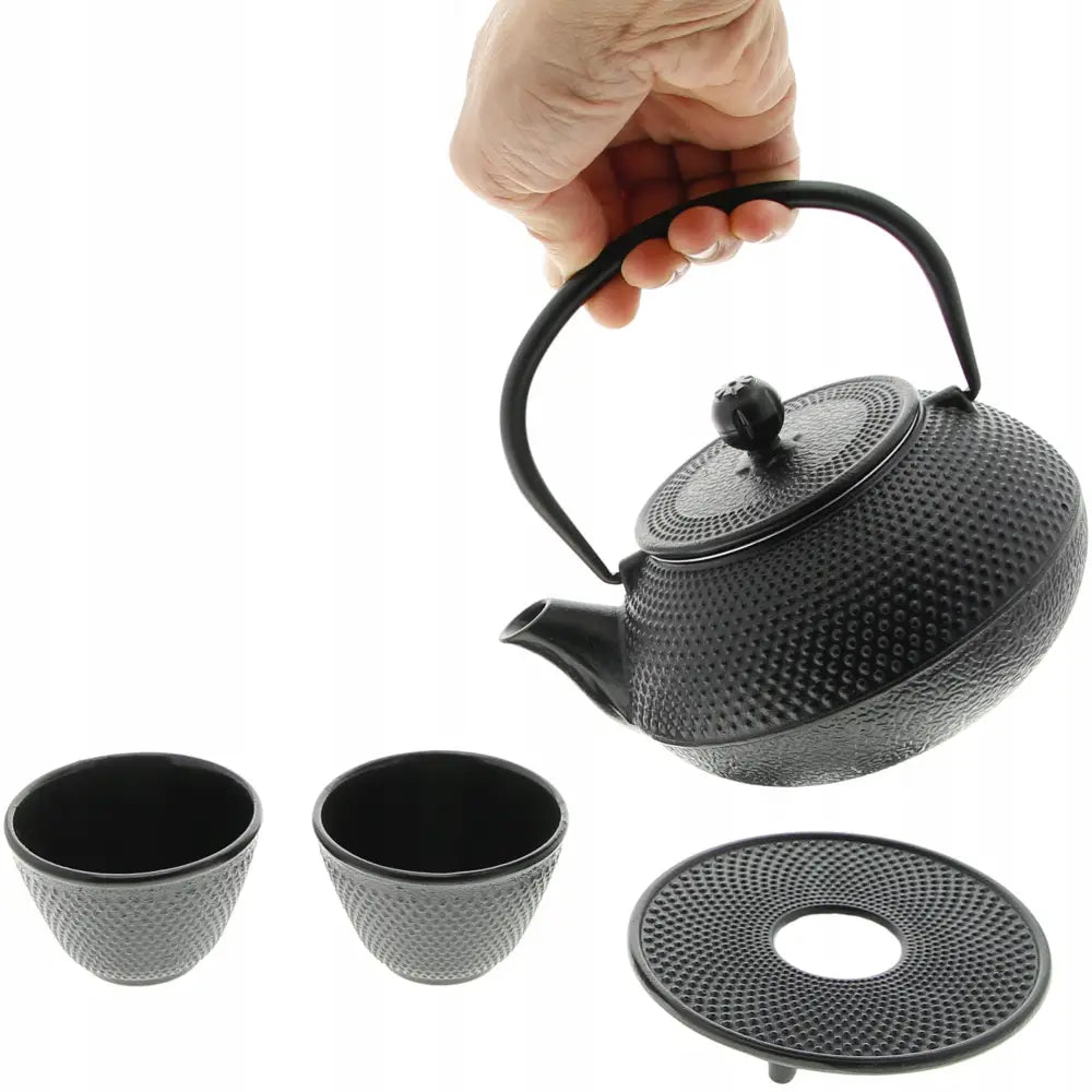 Støpejernsteepot 0,8 L med kopper, skrått sett med rillet tekanne, to kopper og hånd som løfter lokket.