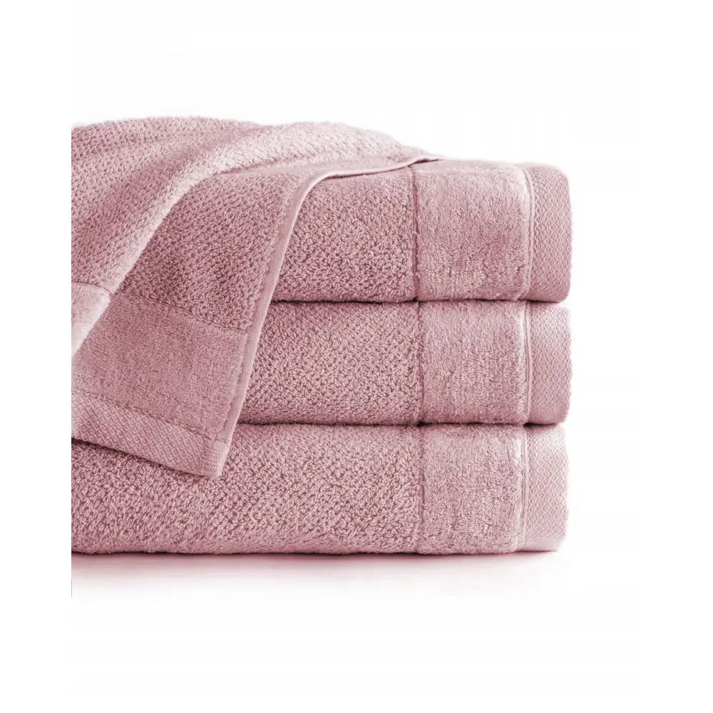 Stort badehåndkle Vito i lyserosa bomull, tre sammenbrettede håndklær med strukturert overflate og kantbånd.