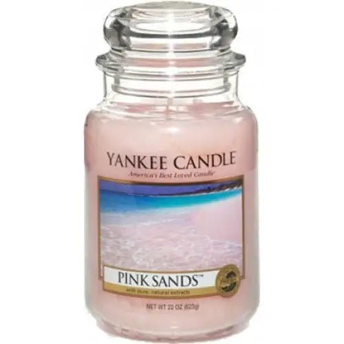 Stort glass rosa sand duftlys, sett forfra med strandetikett og gjennomsiktig lokk.