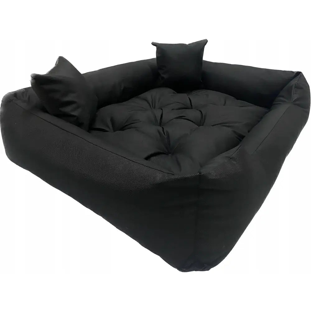 Stort svart hundeseng 130x105 cm med høy kant, to små puter og ekstra polstret bunn, sett fra skrå vinkel.