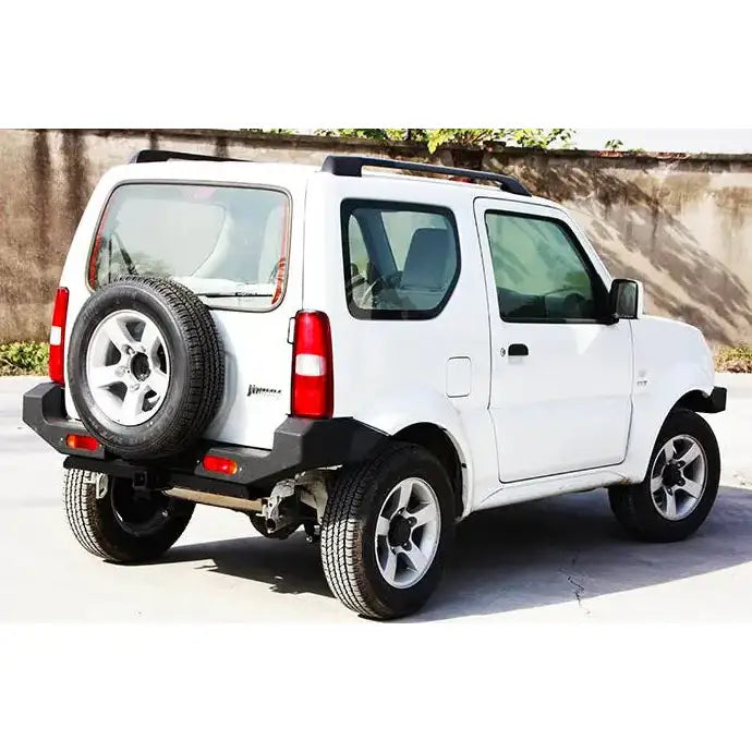 Bakfanger Suzuki Jimny 07-17 på hvit SUV med reservehjul, svarte detaljer og takrails utendørs.