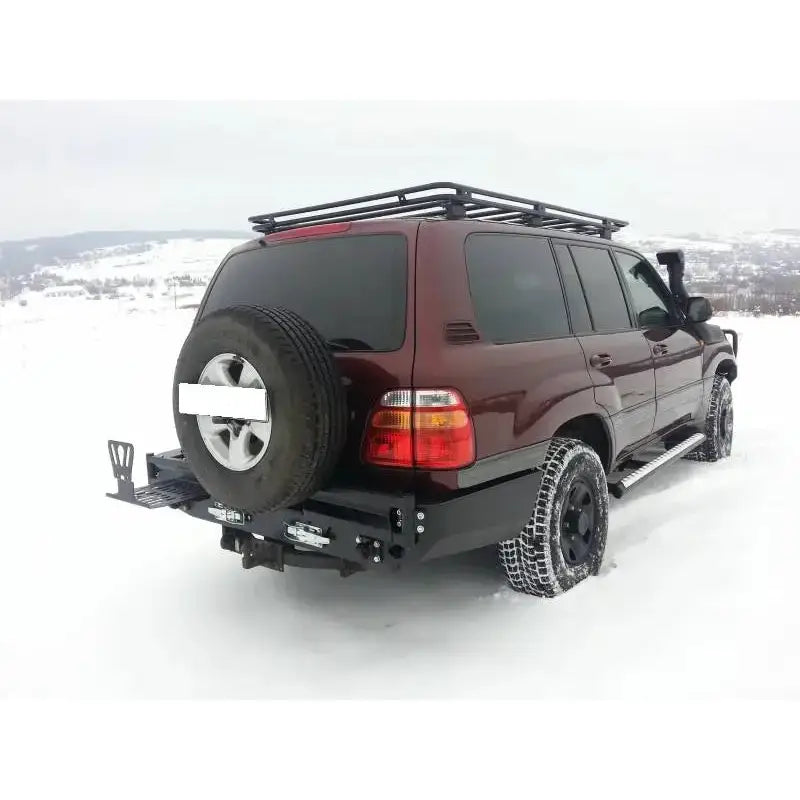 Bakfanger Toyota Land Cruiser J100 montert på mørkerød SUV med takgrind og reservehjul i snødekt landskap.