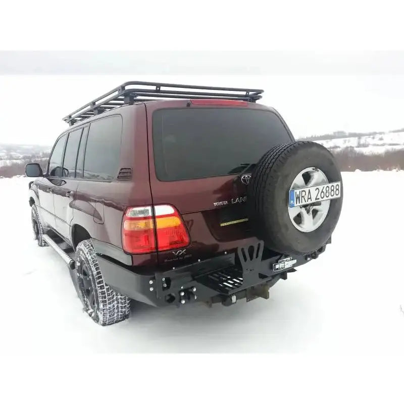 Bakre støtfanger på Toyota Land Cruiser J100 98-07, montert på mørkerød SUV med reservehjul og bagasjebrett.
