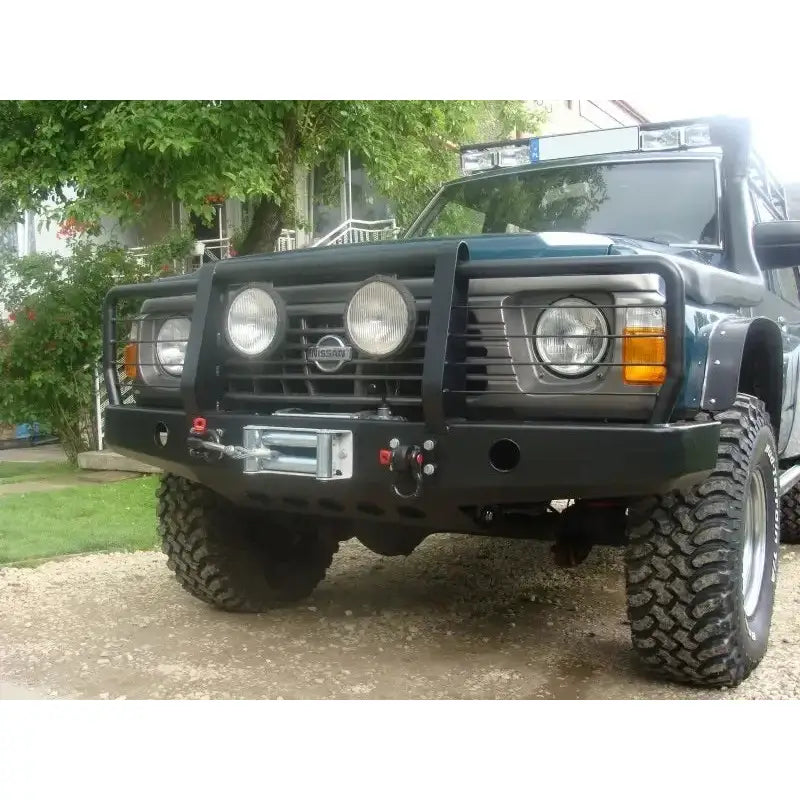 Front bumper på Nissan Patrol Y60 med sort stålfanger, bullbar, vinsj og store runde ekstralys utendørs.