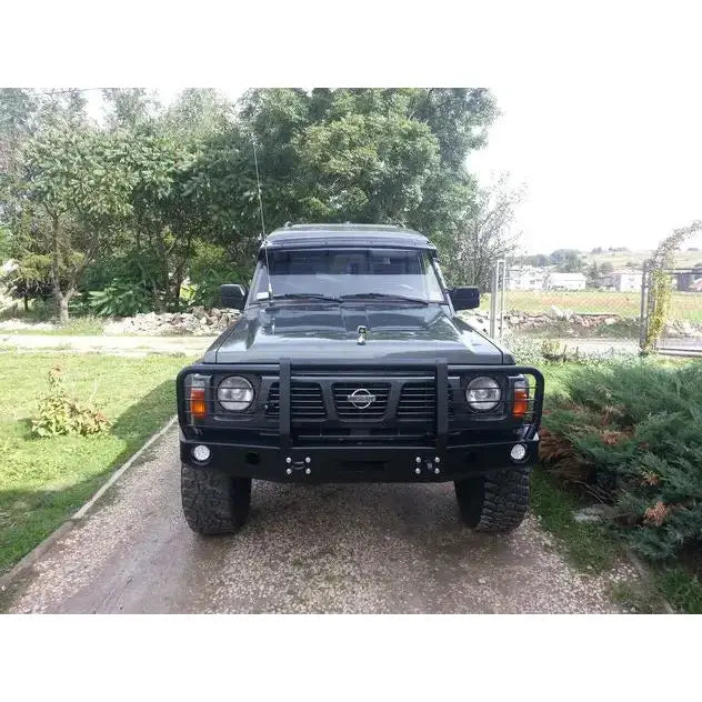 Frontbumper på Nissan Patrol Y60 med bullbar, store dekk og ekstra frontlys på grusvei utendørs.