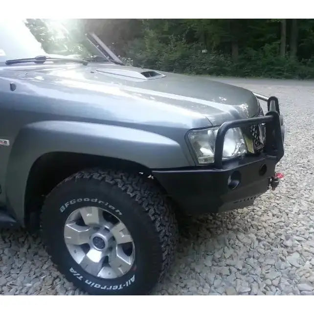 Frontbumper på Nissan Patrol Y61 med svart bullbar, terrengdekk og tydelig frontfanger, parkert på grus.