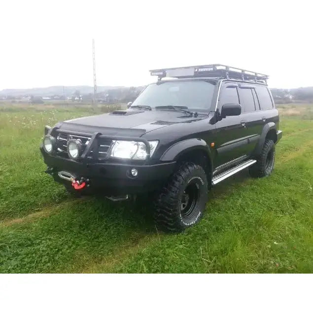 Front bumper på Nissan Patrol Y61 med bullbar, ekstra lykter og store offroad-dekk på gressdekt mark.