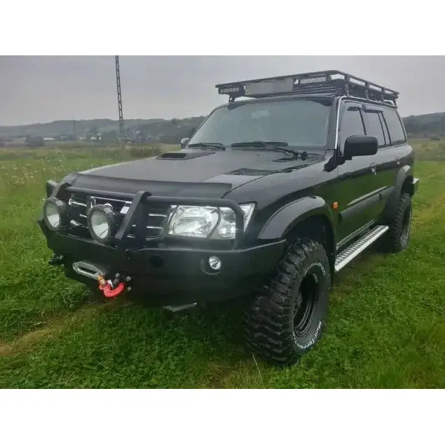 Frontbumper på Nissan Patrol Y61 med bullbar, lyskastere og vinsj, parkert på gressmark.