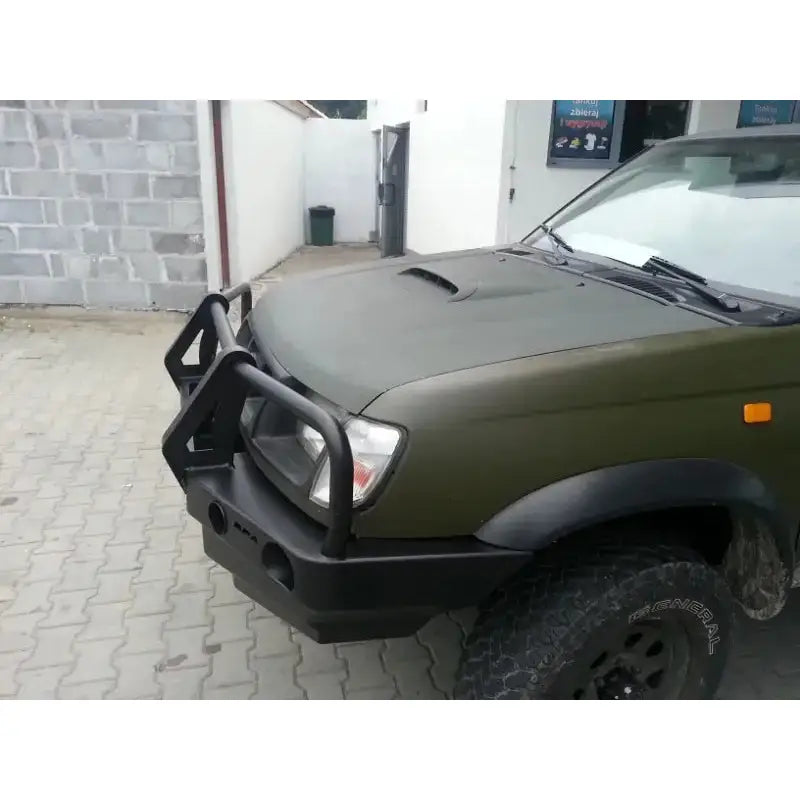 Front bumper på Nissan Pickup D22 97-01 med sort bullbar og robuste terrengdekk fra skrå vinkel.