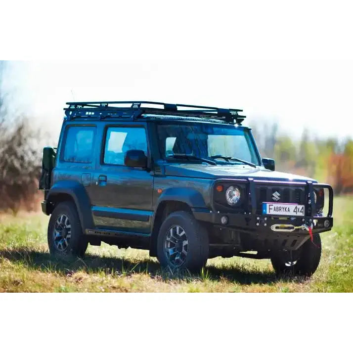 Front bumper på Suzuki Jimny IV med bullbar, takgrind og store hjul, fotografert utendørs på gress.