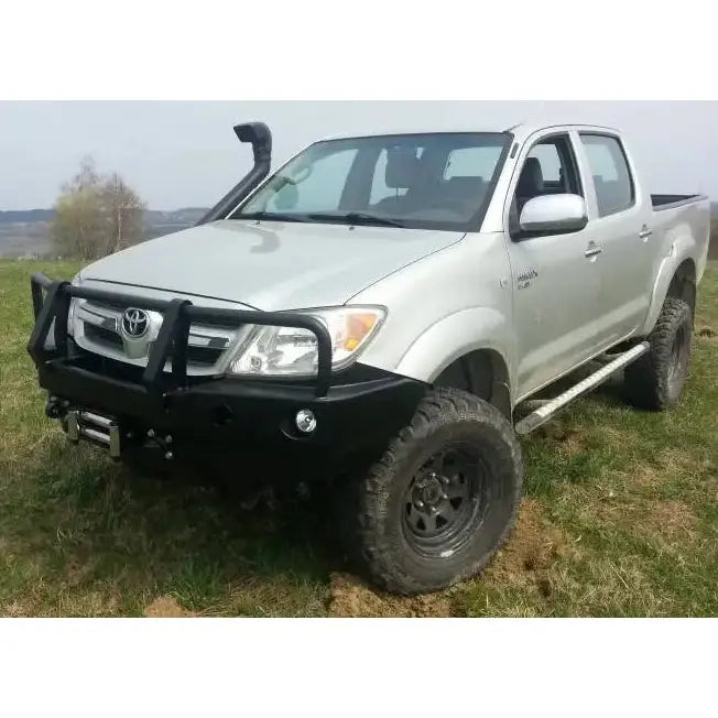 Støtfanger foran med bullbar på sølvfarget Toyota Hilux 05-11 med terrengdekk og snorkel ute i gress.