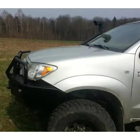 Frontbumper på Toyota Hilux 05-11 med svart bullbar, store terrengdekk og snorkel, sett fra siden.