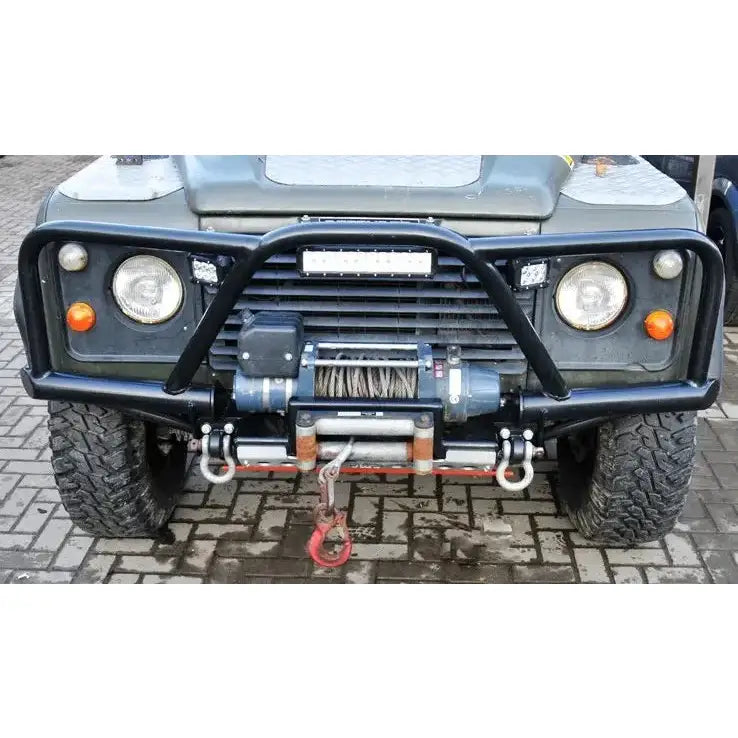 Støtfanger foran Land Rover Defender med bullbar, vinsj, tau og krok på brosteinslagt underlag.