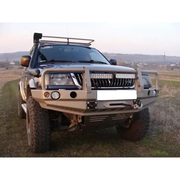 Frontfanger Mitsubishi Pajero Sport 96-00 i beige metall med beskyttelsesbøyle og ekstra lys utendørs.