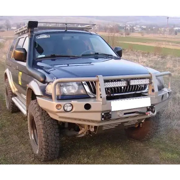 Front bumper på Mitsubishi Pajero Sport 96-00 med beige kufanger, takstativ og terrengdekk utendørs.