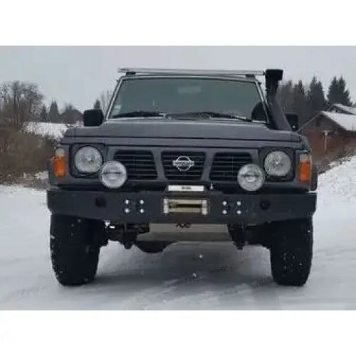 Frontfanger på Nissan Patrol Y60 med fire runde ekstralys, vinsj og snorkel i snødekt terreng.