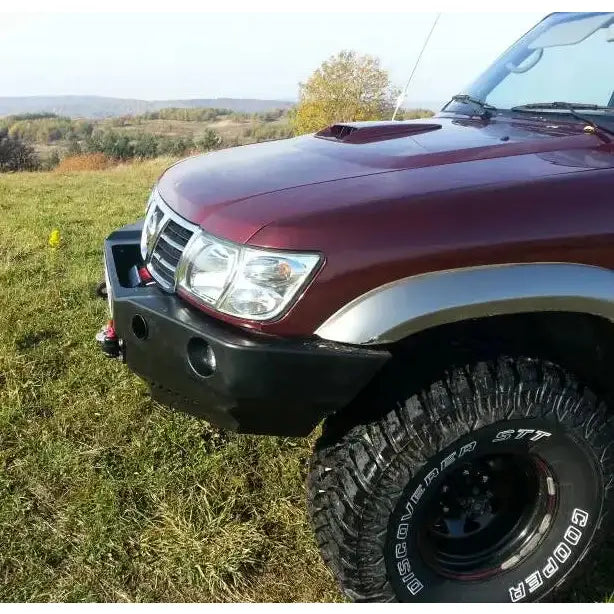 Frontbumper til Nissan Patrol Y61 97-04 montert på mørkerød SUV med store terrengdekk utendørs.