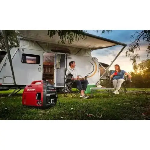 Strømaggregat Honda EU22i på gress ved campingvogn, to personer i stoler ved siden av, ute i naturen.