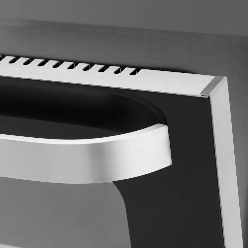Stykke konveksjonsovn, nærbilde av håndtak i børstet stål og ventilert list på sort og sølvfarget panel.