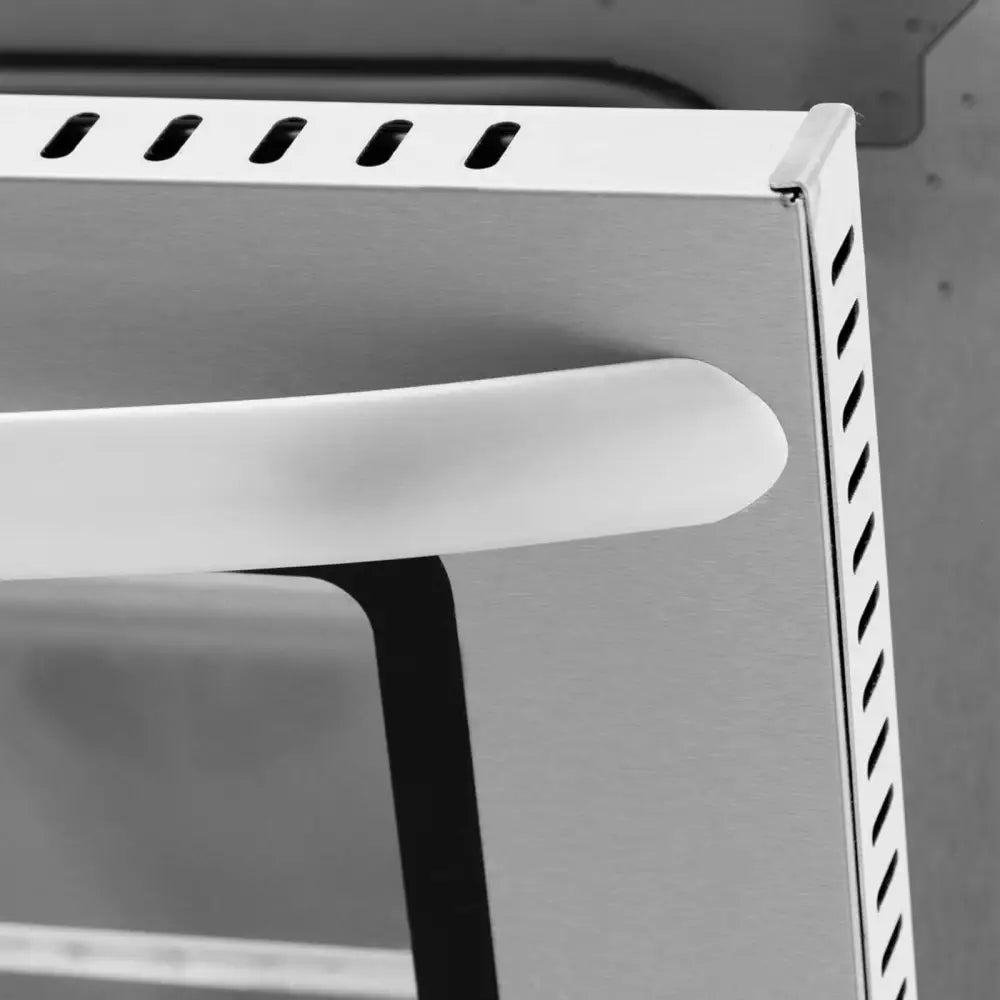 Stykke konveksjonsovn, detalj av ovnsdørhjørne i rustfritt stål med hvitt håndtak og luftehull.