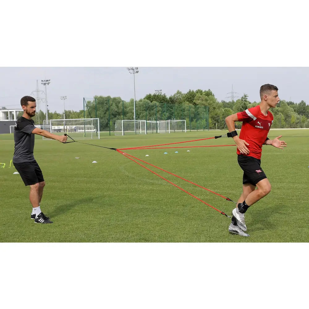 Styrketreningsgummi Edderkopp, rødt motstandsbånd festet mellom to personer under utendørs trening på gress.