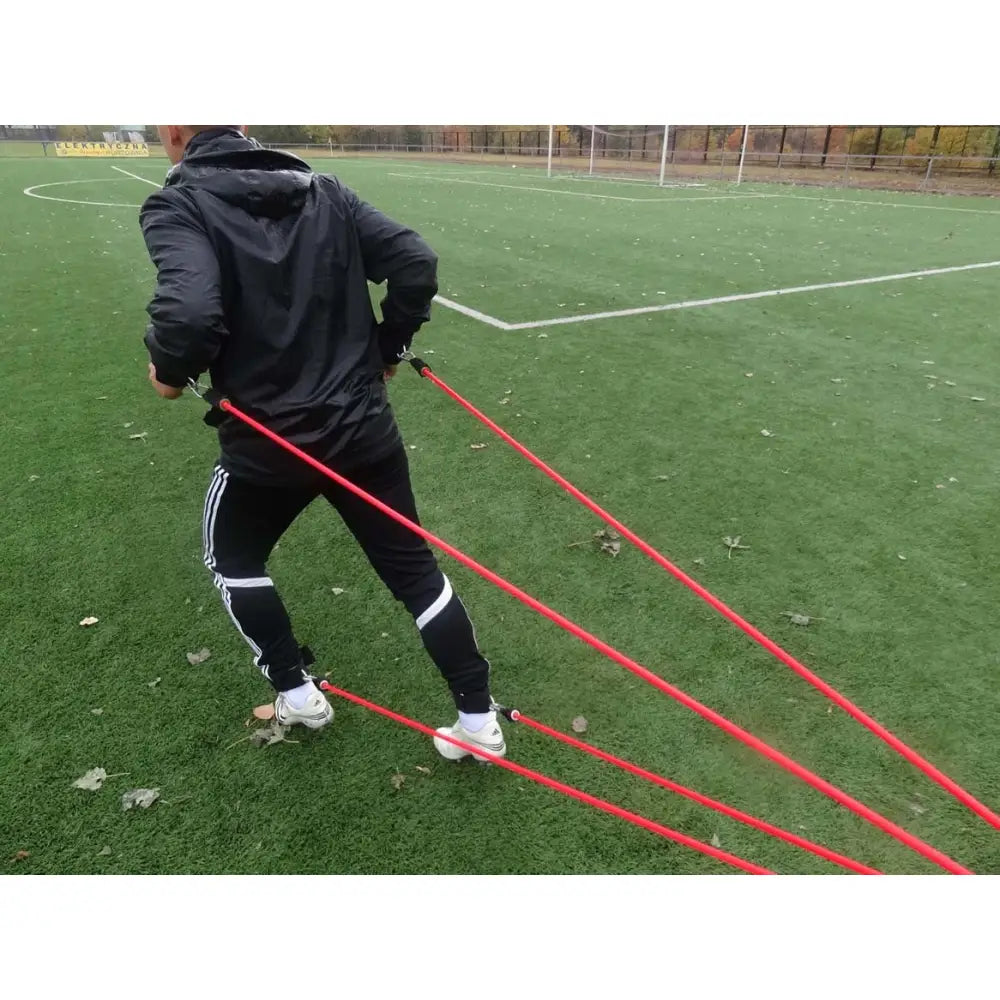 Styrketreningsgummi Edderkopp i bruk utendørs, strikkene festet rundt liv og ankler på fotballbane.