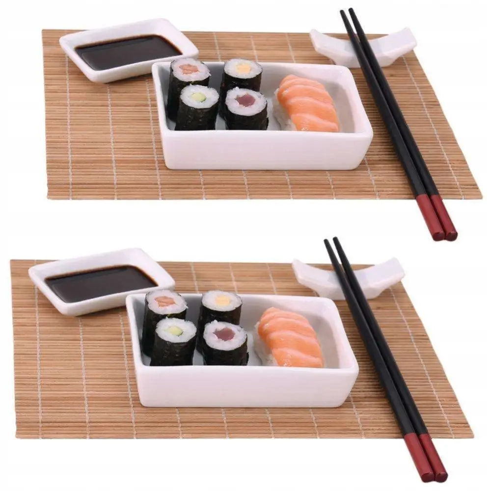 Sushi serveringssett for to, med bambusmatte, hvite skåler, svarte spisepinner og assortert sushi sett ovenfra.