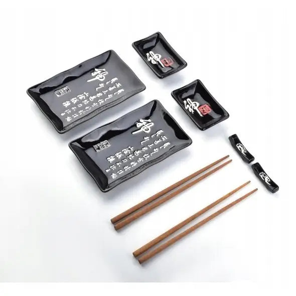 Sushisett for to med sorte keramiktallerkener, små skåler, spisepinner og holdere med hvite tegn.