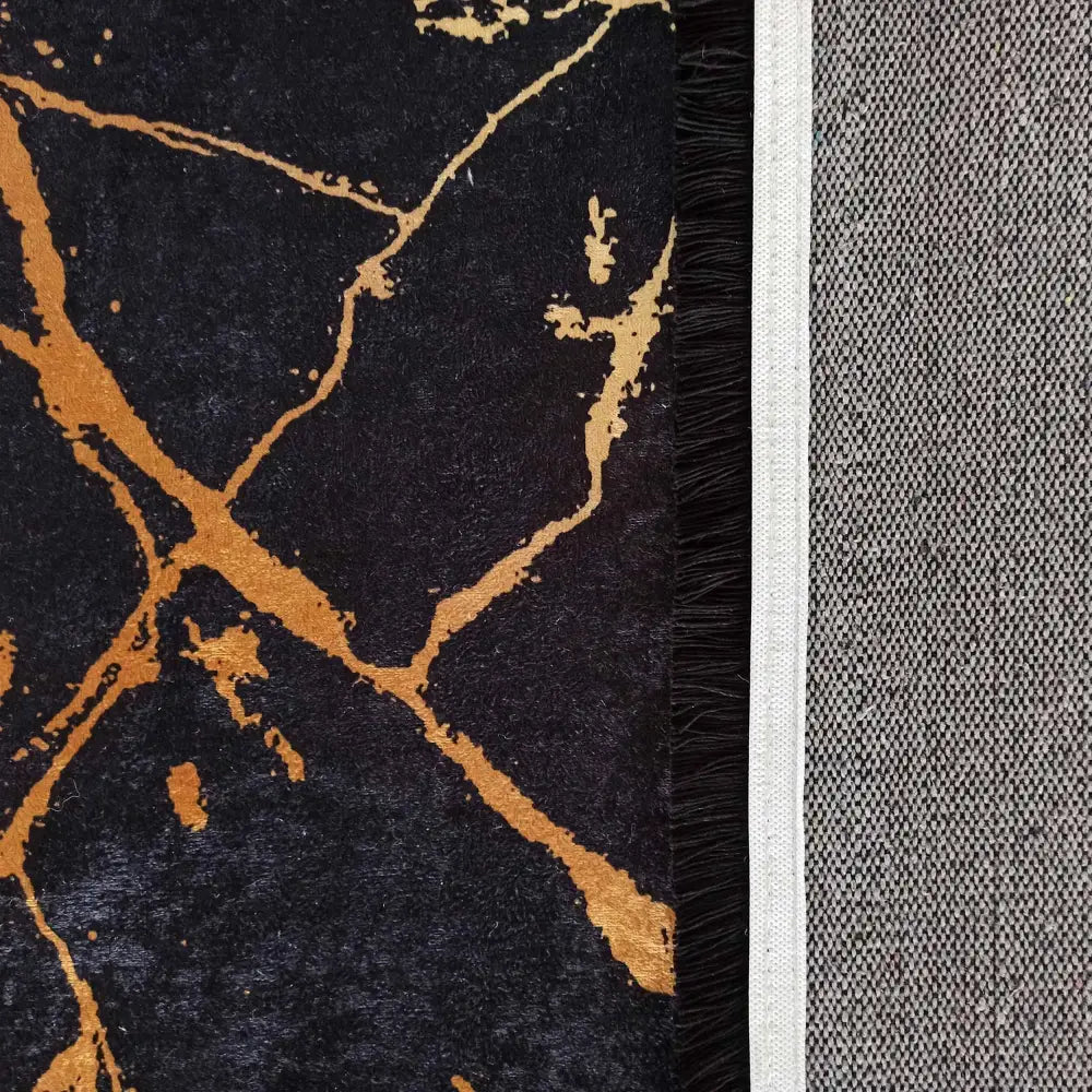 Svart og gull teppe 120 x 180 cm, nærbilde av marmorerte oransje linjer og sorte frynser mot grå underside.
